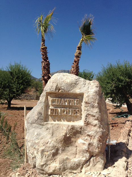 Cuatre Finques stone entrance sign among almond and palm trees